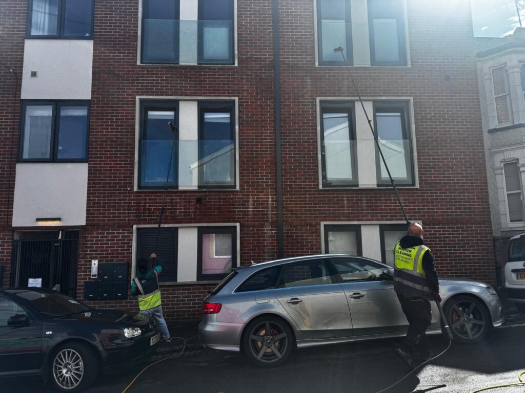 Two AquaClean operatives cleaning windows on a brick apartment building