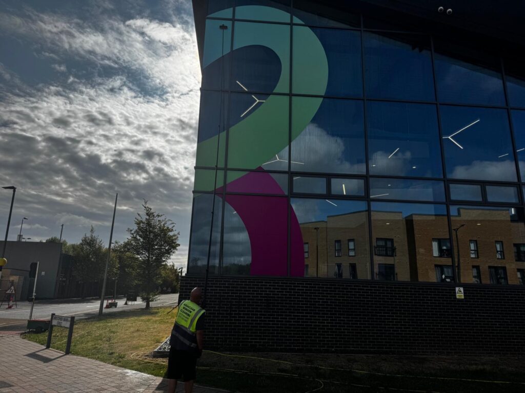 Window-cleaning pole in use on a glazed frontage with coloured panels